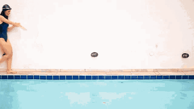 a woman in a blue swimsuit is walking towards a pool