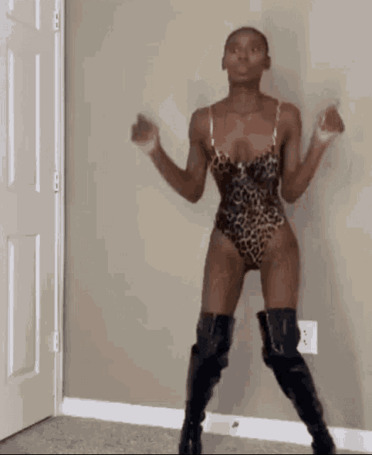 a woman in a leopard print bodysuit and black boots is standing in a room .