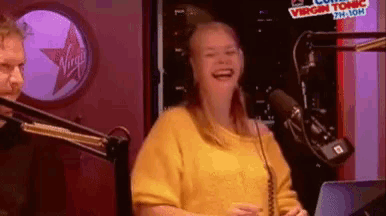 a woman in a yellow sweater is laughing in front of a microphone .
