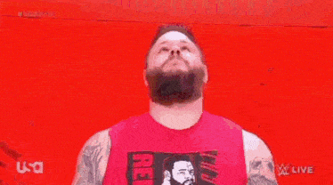 a man with a beard is screaming in front of a red wall while wearing a red tank top .