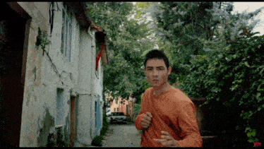 a man in an orange shirt is walking down a narrow alleyway