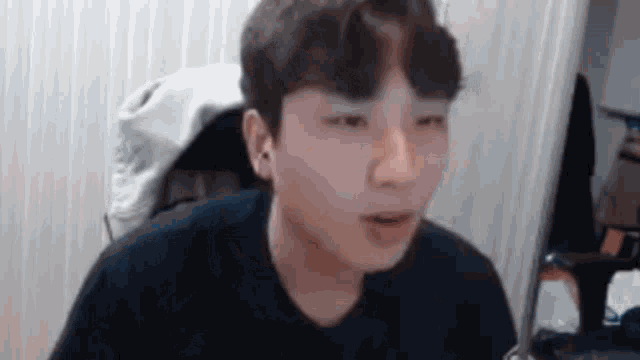 a young man in a black shirt is sitting in front of a computer screen and making a funny face .