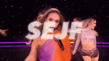 a woman sings into a microphone with the word self behind her