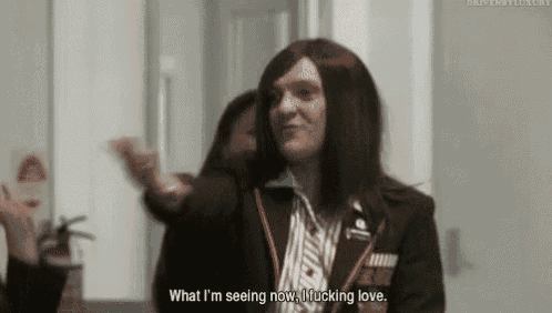 a man with long hair and a wig is talking to a woman in a room .