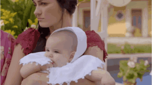 a woman is holding a baby in her arms who is wearing a white hat