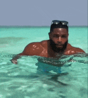 a man with a beard is swimming in the ocean wearing sunglasses