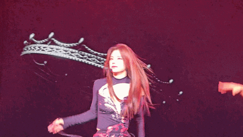 a woman in a purple top is dancing on a dark stage