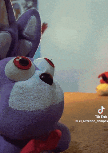 a purple stuffed animal with red eyes and a red bow on its mouth