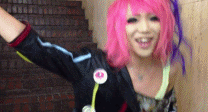 a woman with pink hair is wearing a black jacket and smiling .
