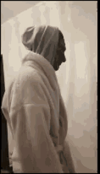 a man wearing a white robe and a hooded sweatshirt is standing in a bathroom .
