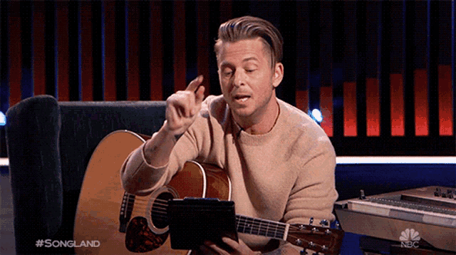 a man holding a guitar and a tablet with the words #songland on the bottom