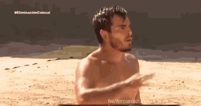 a shirtless man is standing on a sandy beach with the words eliminacion colosal on the bottom right