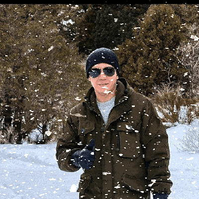 a man standing in the snow wearing sunglasses and a hat