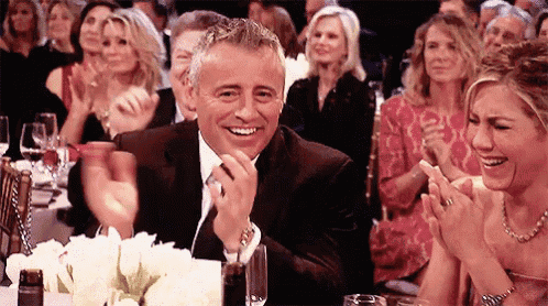 a man in a suit and tie is smiling while sitting at a table with other people applauding .