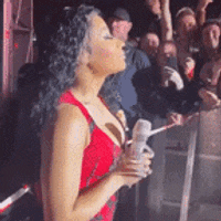 a woman in a red dress is standing in front of a crowd holding a remote control .