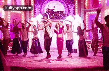 a group of people are dancing on a stage in front of a pink background .