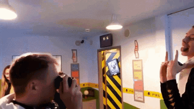 a man is taking a picture of another man in a room with a clock that says 8.6