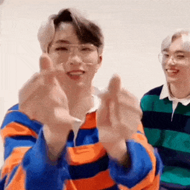 a man wearing glasses and a striped shirt is making a heart with his hands .