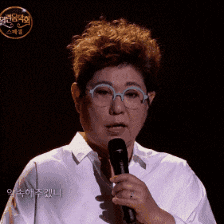 a woman wearing glasses and a white shirt holds a microphone in her hand