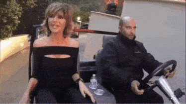 a woman in a black dress is sitting next to a man in a black jacket driving a golf cart .