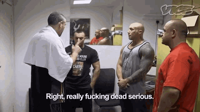 a man wearing a t-shirt that says cartel is talking to two other men