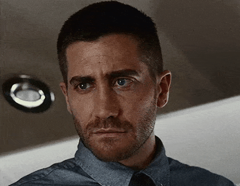 a close up of a man 's face with a beard wearing a blue shirt and tie .
