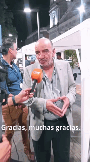 a man is talking into a microphone with the words gracias muchas gracias behind him