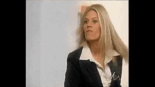a woman in a suit and white shirt is standing in front of a white wall .