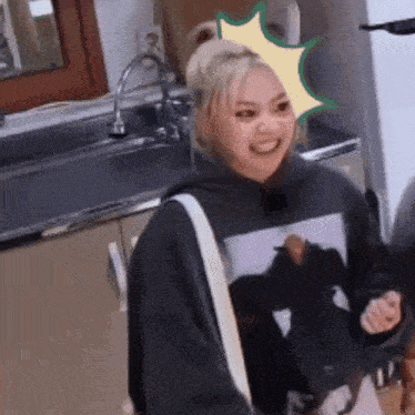 a woman in a black hoodie is standing in a kitchen with a sticker on her head .