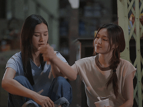 two women are sitting next to each other holding hands and one is holding a cup that says ' strawberry ' on it