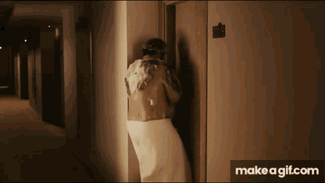 a man wrapped in a towel is washing his back in a hallway next to a door .