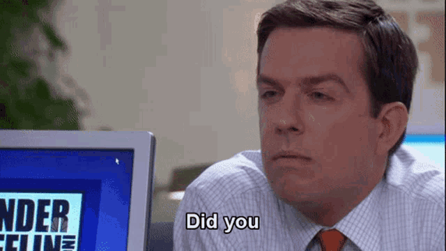 a man in a suit and tie is sitting in front of a computer monitor and says did you .