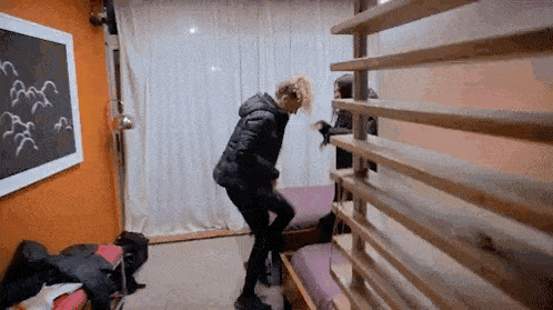 a man in a black jacket is standing next to a wooden fence in a bedroom .