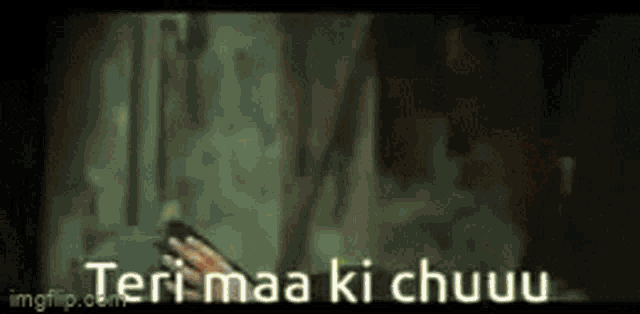 a person is holding a cell phone in a dark room with the words teri maa ki chuuu written on the screen .