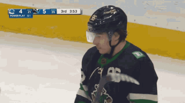 a hockey player stands on the ice with a scoreboard behind him