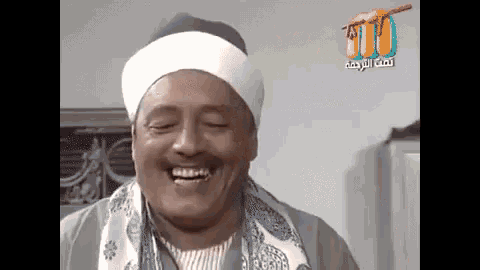 a man wearing a turban and a scarf is smiling in front of a sign that says ' tnt '