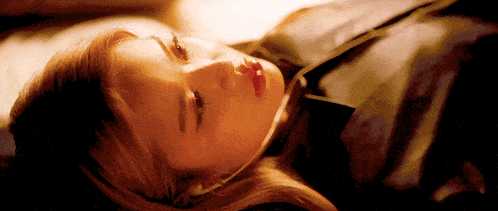 a woman laying down with her eyes closed and a black jacket on