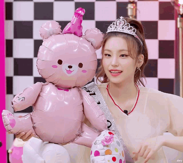 a girl wearing a tiara and holding a pink teddy bear balloon