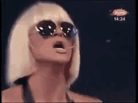a woman wearing sunglasses and a blonde wig is making a funny face .