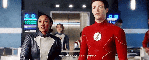 a man and a woman are standing next to each other in a room in a flash suit .