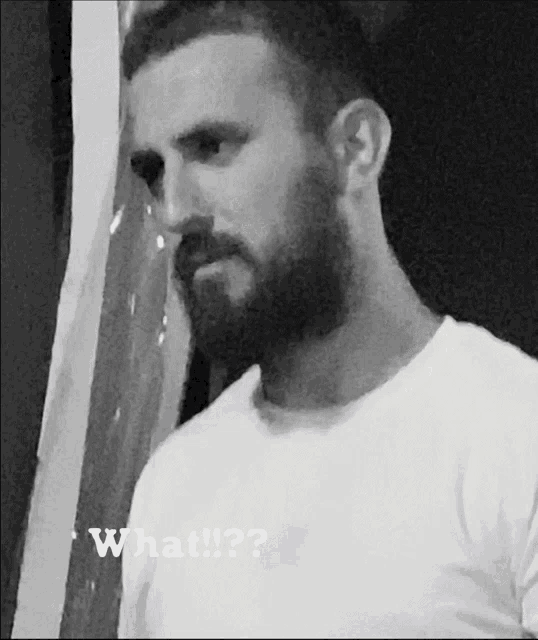 a man with a beard is wearing a white shirt and has the word what on the bottom right