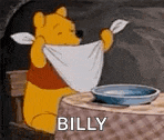 winnie the pooh is sitting at a table holding a towel around his neck and saying `` billy '' .