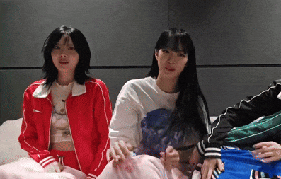 two girls are sitting next to each other on a bed and one of them is wearing a red jacket