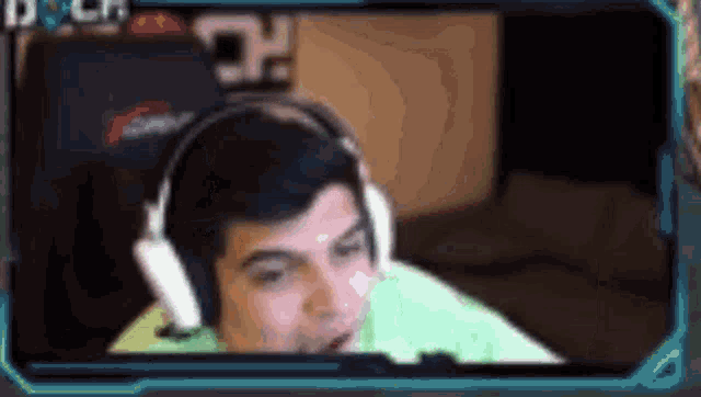 a man wearing headphones and a green shirt is sitting in front of a computer screen .