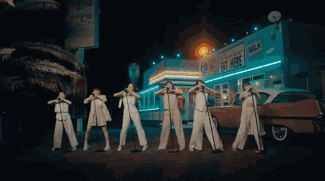 a group of women singing in front of a diner that has a sign that says dairy eat here