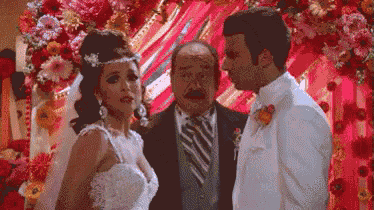 a bride and groom are standing next to each other in front of a floral arch .