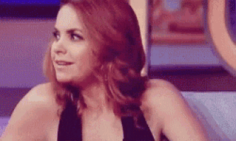 a woman with red hair and a black dress is sitting on a couch and smiling .