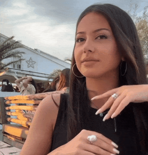 a woman wearing hoop earrings and a ring on her finger looks at the camera