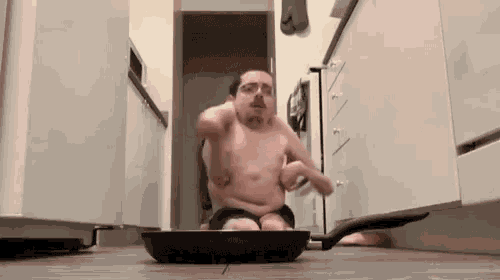 a shirtless man is sitting on a frying pan in a kitchen ..
