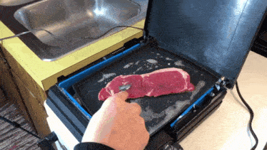 a person is cooking a steak on a griddle in a kitchen